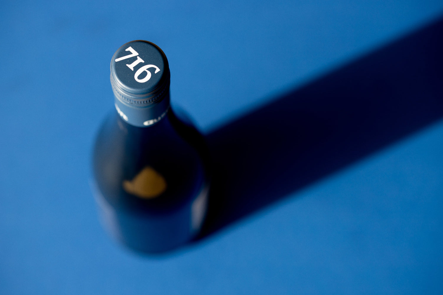 716 Rotwein Flasche mit blauer Kapsel mit weißem Aufdruck 716 von oben fotografiert auf blauem Hintergrund.